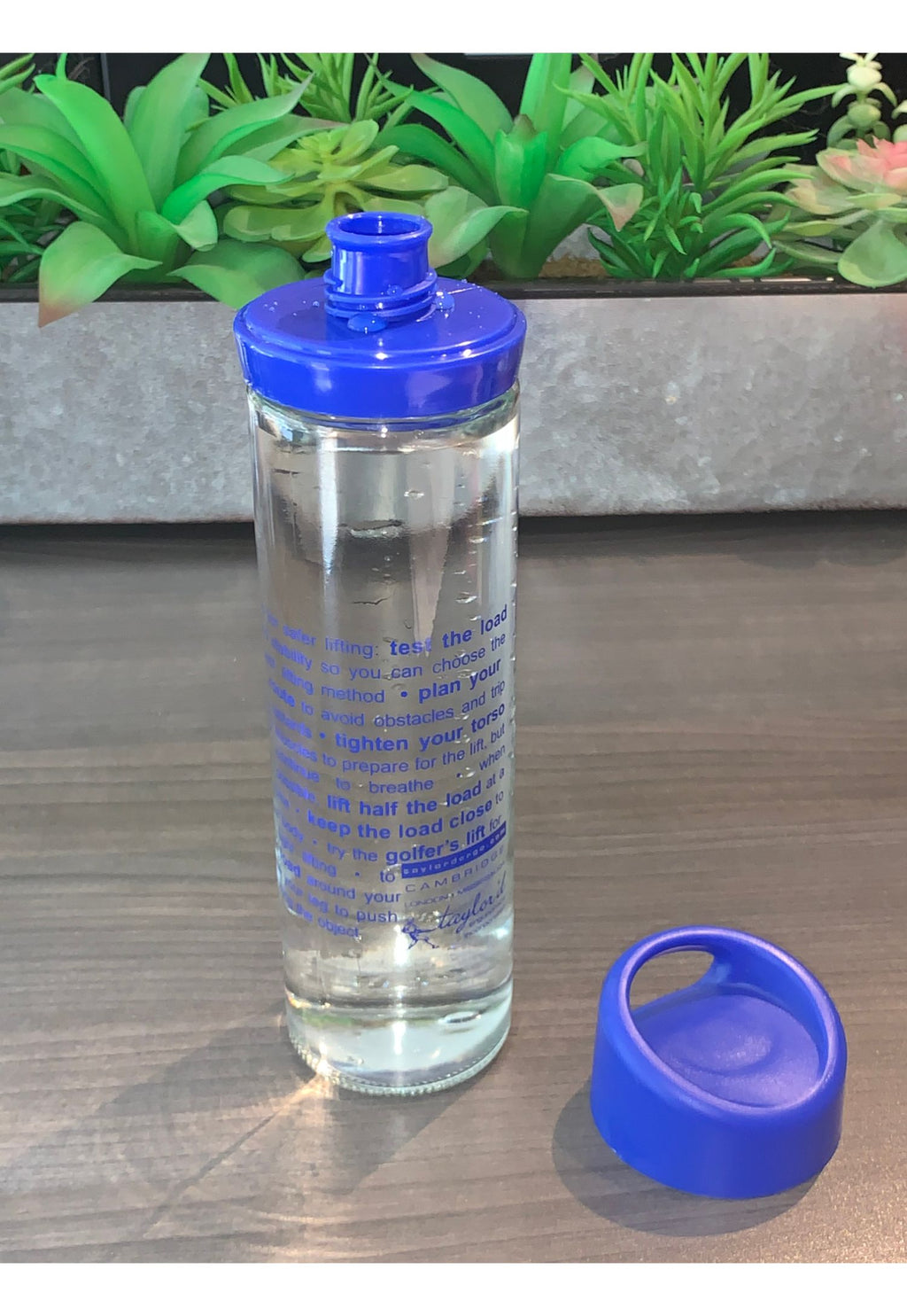 photograph of glass water bottle with blue lid and spout, showing ergonomics lifting tips imprint